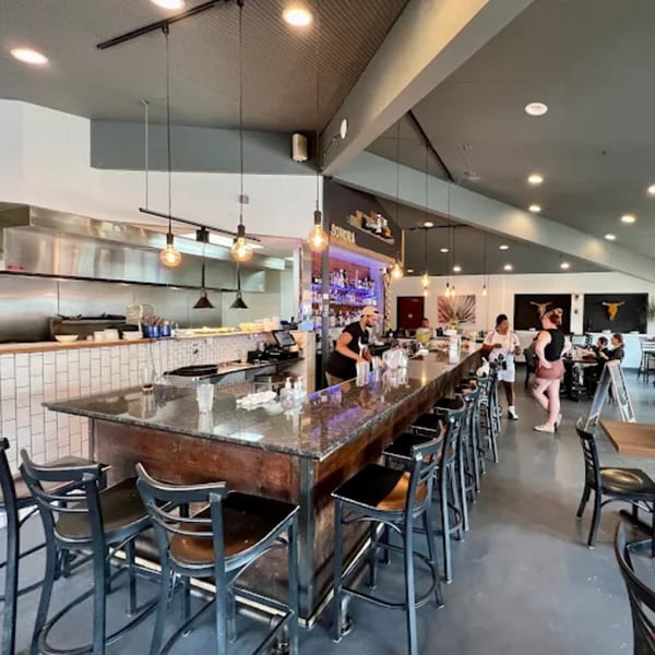 Sonora Grill's interior with a long bar, open kitchen, and patrons enjoying the vibrant atmosphere.