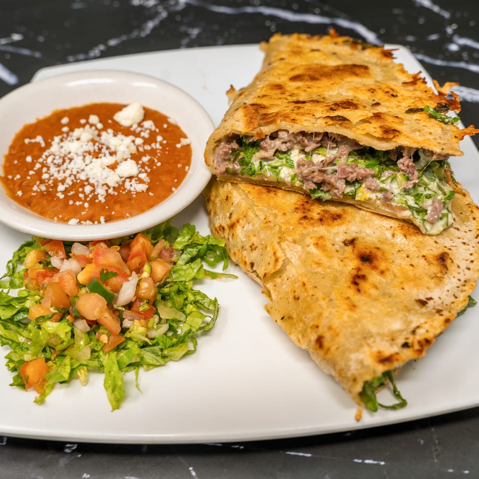 A large, golden-brown quesadilla filled with meat and cheese, served with refried beans and pico de gallo.
