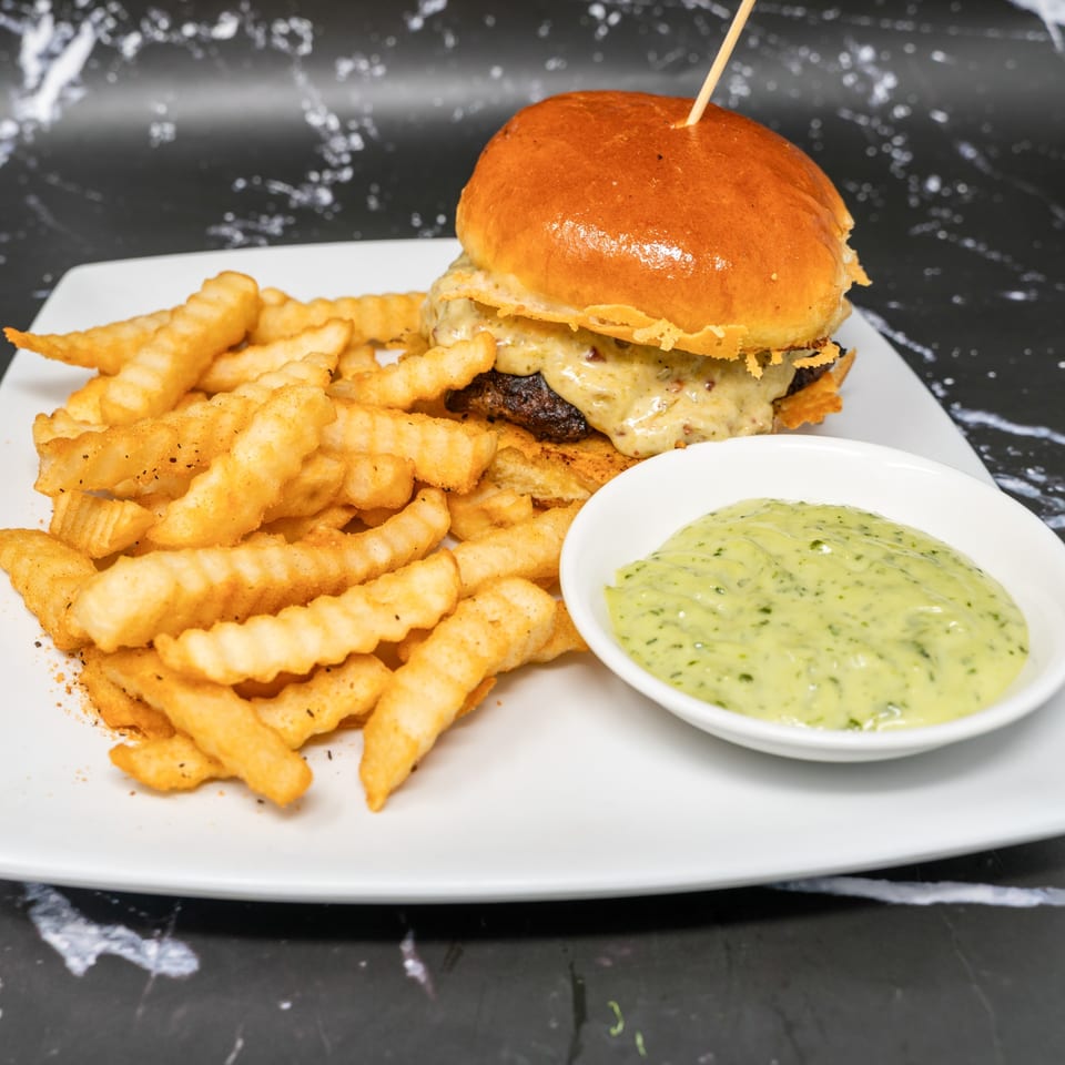 Cheeseburger with crinkle-cut fries and a side of green dipping sauce on a white plate.