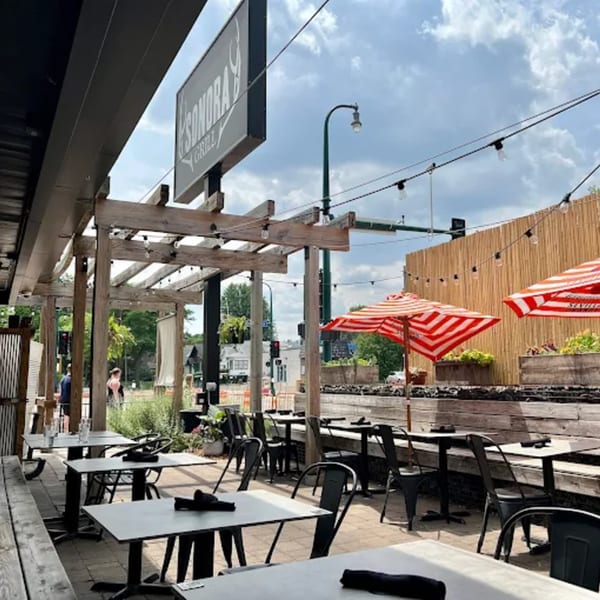 Sonora Grill's outdoor patio with tables, chairs, red and white striped umbrellas, and string lights.