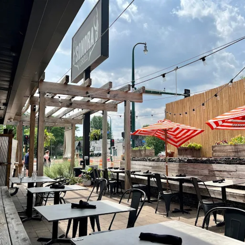 Sonora Grill's outdoor patio with tables, chairs, red and white striped umbrellas, and string lights.