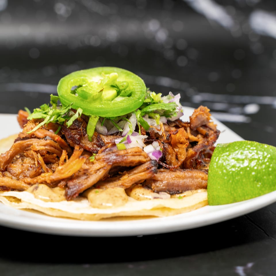 A Sonora Grill taco with shredded meat, cilantro, onions, and jalapeño, served with a lime wedge.