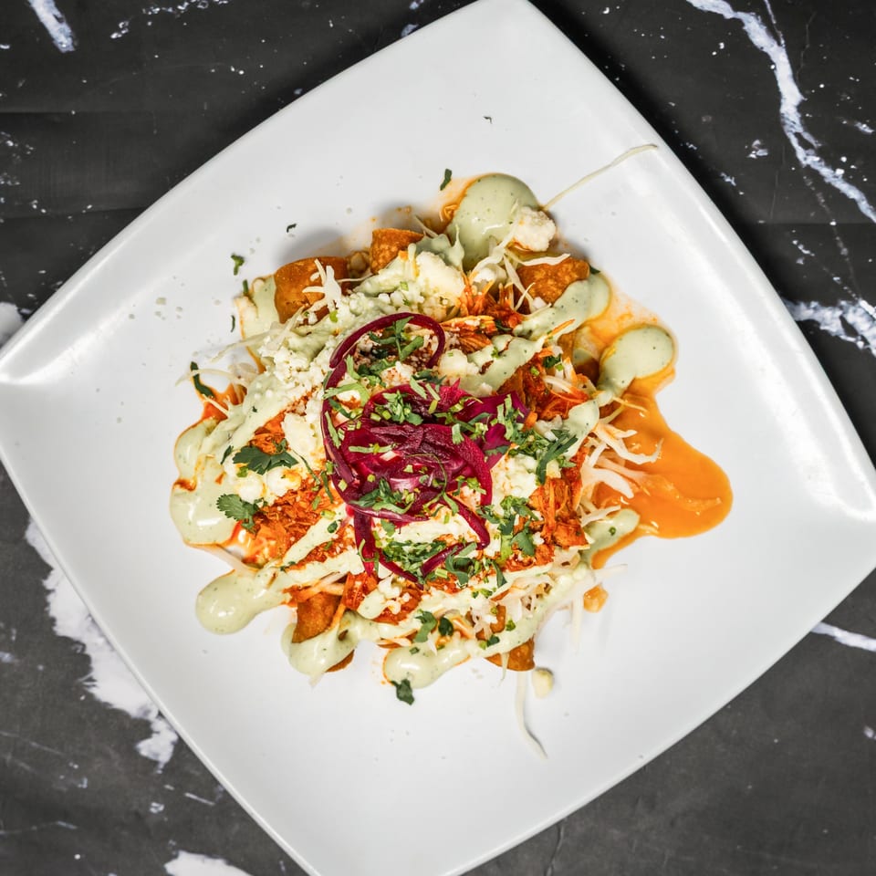 Top-down view of Sonora Grill's Mexican dish with red sauce, green crema, cheese, and cilantro.