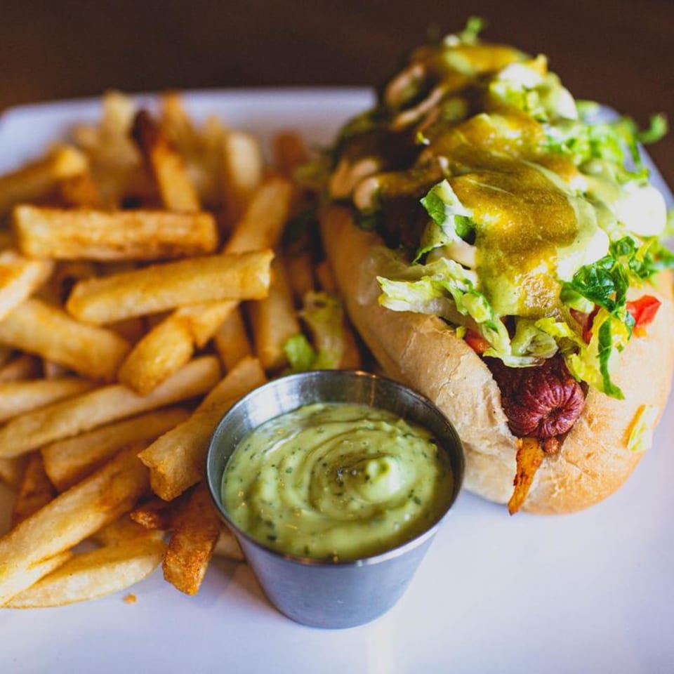Sonora Grill's hot dog with lettuce, sauce, and fries, served with a side of green dip.