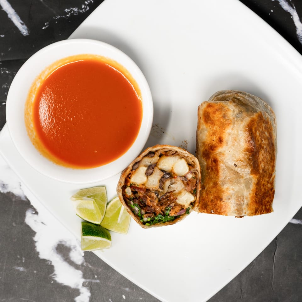A Sonora Grill burrito, cut in half to show the filling, with a side of red sauce and lime wedges.