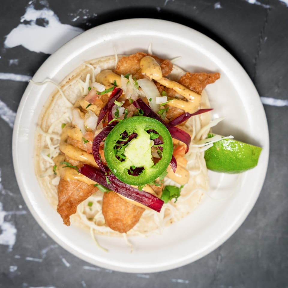 Top-down view of a Sonora Grill fish taco with fried fish, cabbage, sauce, red onion, and jalapeño.